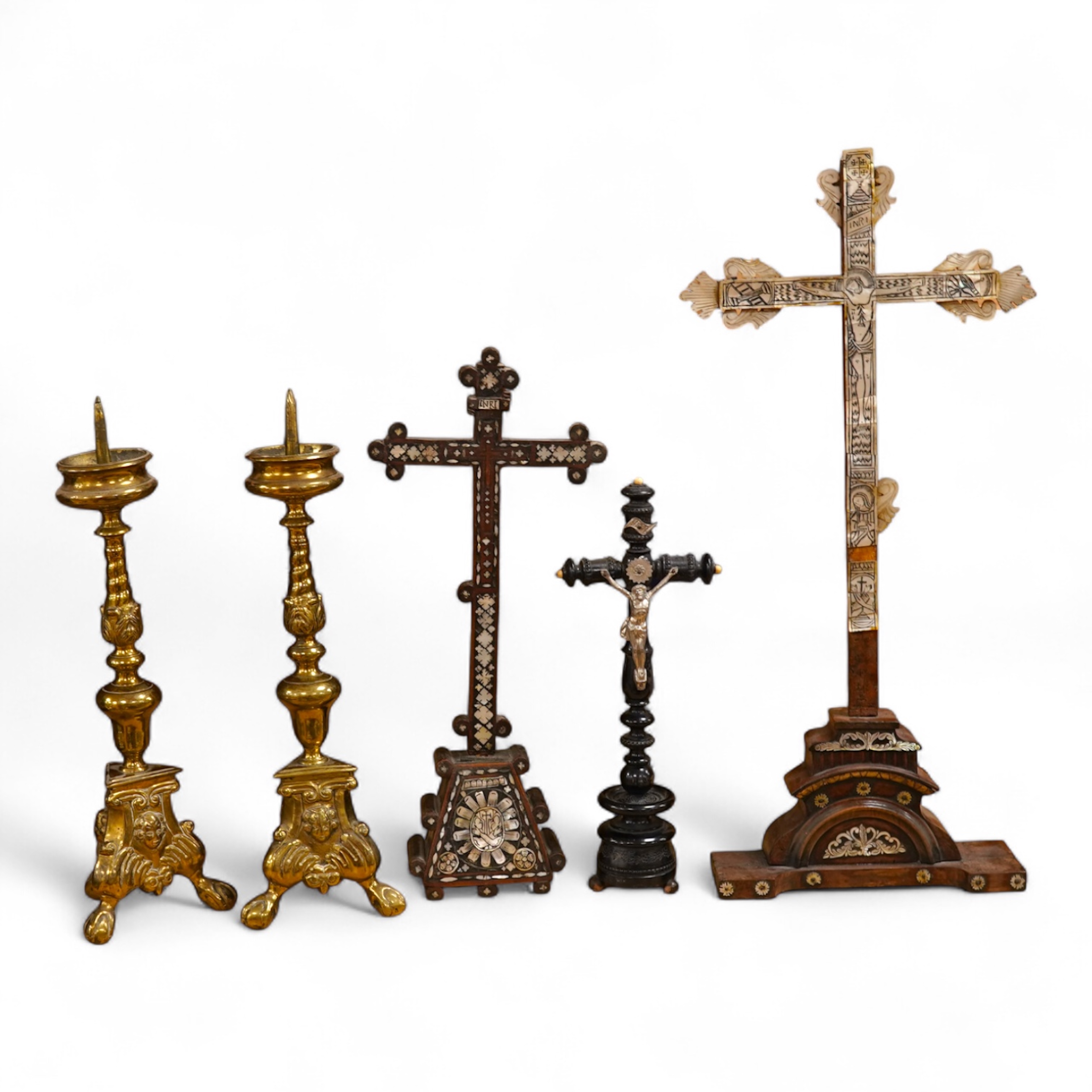 Two 19th century walnut and mother-of-pearl inlaid crucifixes and a German ebonised and white and metal mounted crucifix and a pair of Dutch or German brass tripod base cricket candlesticks, largest 56cm high (5)